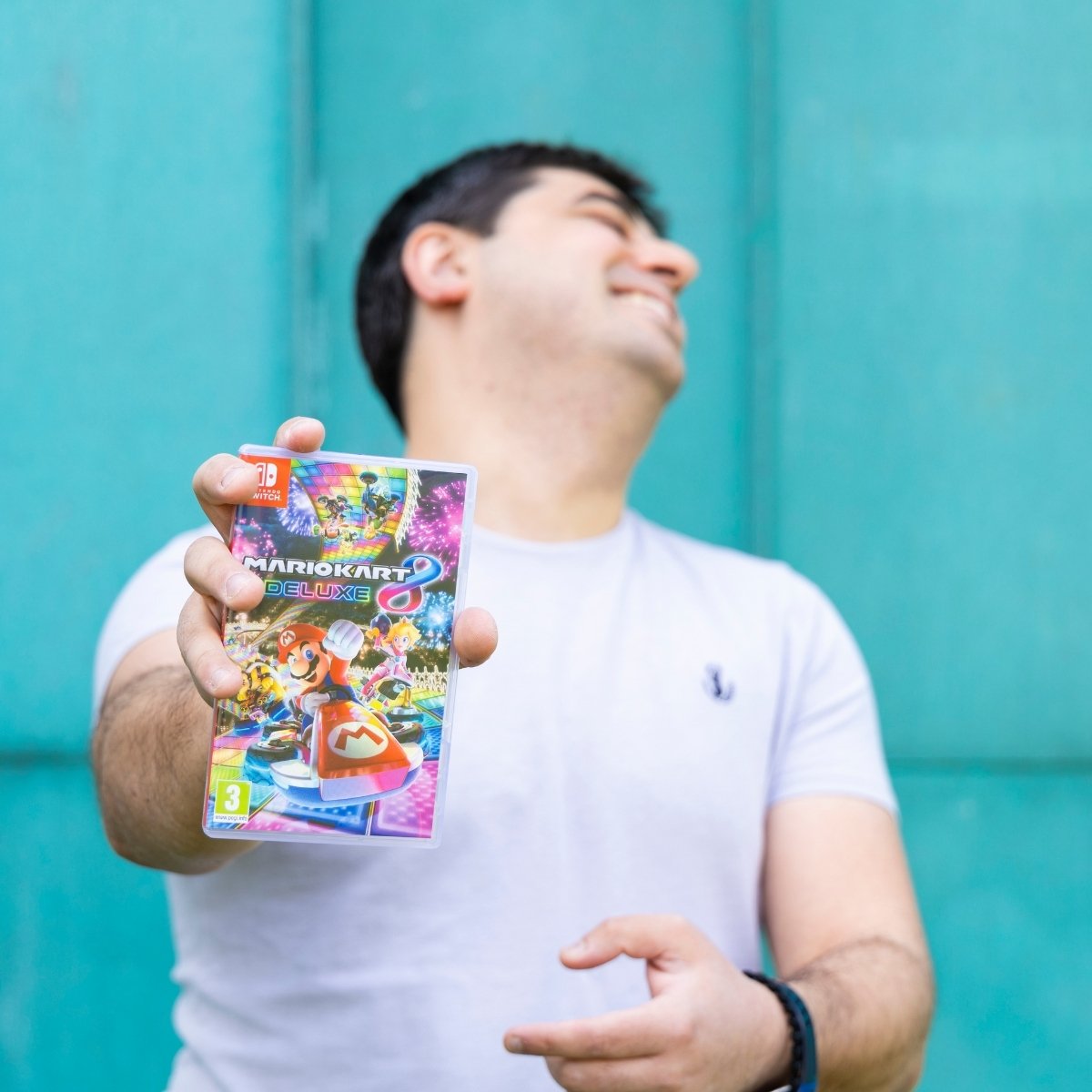 Team Photos - Archimedia Accounts - individual headshot in front of a bright blue wall holding out a Nintendo Switch game - Chris Demetriou