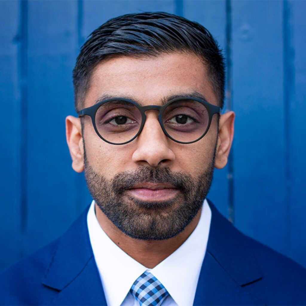 Headshot of male against bright blue background. My client wears thick rimmed glasses and looks directly into the camera with a very slight smile.